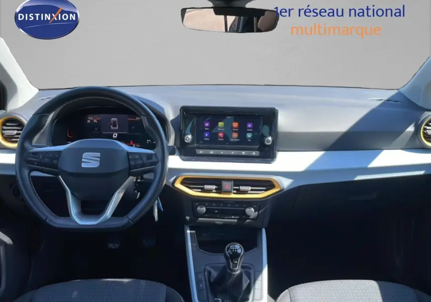 Vue intérieure avant du SEAT Arona 2025, tableau de bord gris clair avec touches dorées et volant multifonction noir.