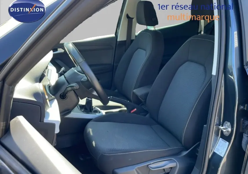 Vue intérieure côté conducteur du SEAT Arona 2025, sièges tissu gris foncé et volant cuir multifonction.