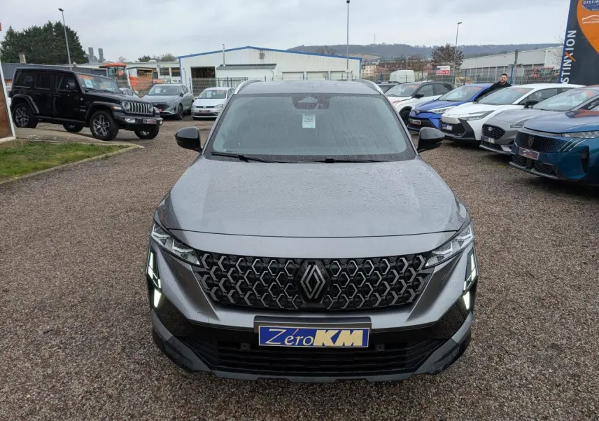 Vue avant d'un Renault Austral gris avec calandre hexagonale et feux LED allumés sur un parking extérieur.