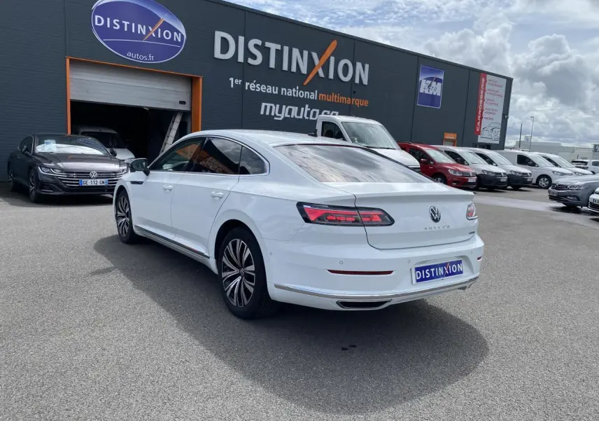 Vue 3/4 arrière droite d'une Volkswagen Arteon blanc pur avec feux arrière LED et jantes alliage sur parking extérieur.