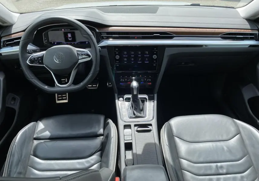 Vue intérieure avant du Volkswagen Arteon 2022, sellerie cuir noir, tableau de bord avec écran tactile et volant multifonction.