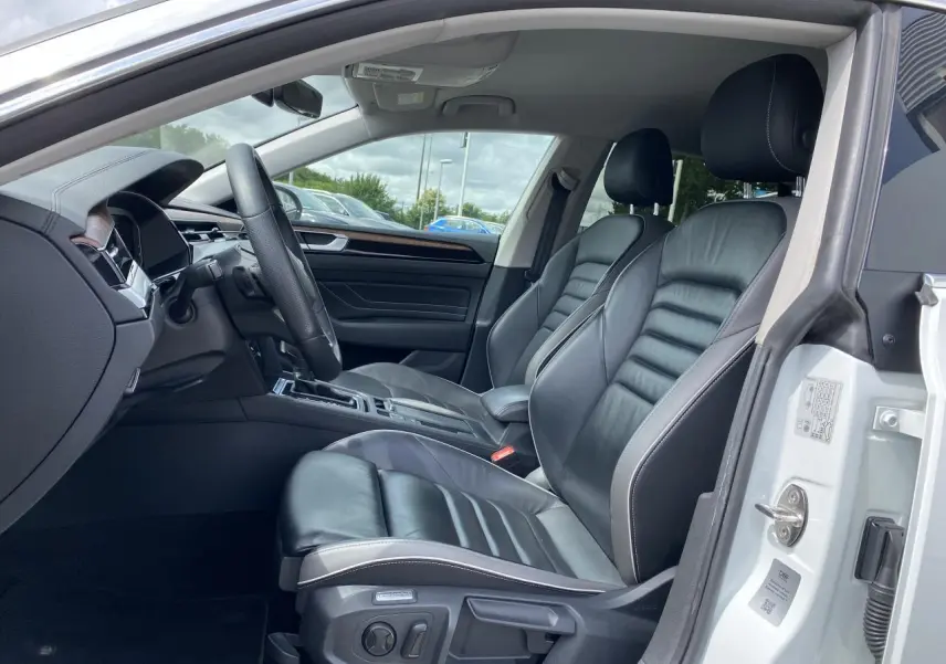 Vue intérieure côté conducteur du Volkswagen Arteon blanc pur 2022, sièges avant en cuir Nappa noir avec finitions bois précieux.