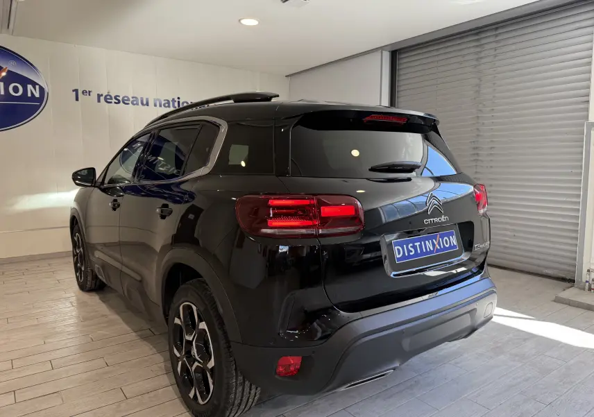 Vue 3/4 arrière droite d'un Citroën C5 Aircross noir brillant en showroom avec feux arrière allumés.