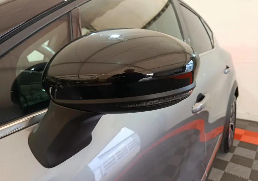 Gros plan sur le rétroviseur noir côté gauche du Renault Captur gris foncé, avec partie avant du véhicule visible.