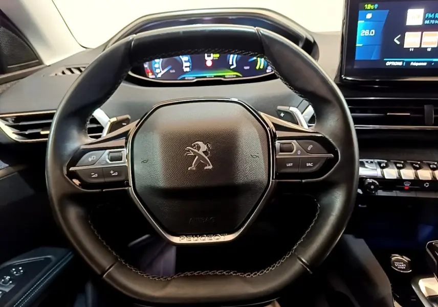 Vue rapprochée du volant cuir noir du Peugeot 3008 1.6 Hybrid 225, avec commandes multifonctions et tableau de bord digital.