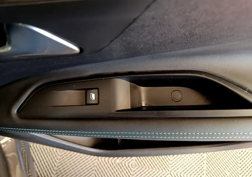 Gros plan sur la commande de lève-vitre côté conducteur avec surpiqûres bleues sur la garniture intérieure noire.
