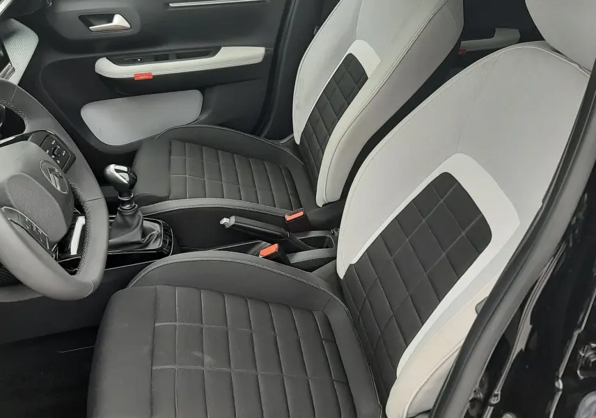 Vue intérieure côté conducteur de la Citroën C3 2025, sièges bi-matière noir et blanc avec coutures apparentes.