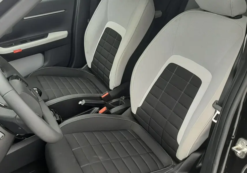 Vue intérieure en gros plan des sièges avant bi-matière noir et blanc de la Citroën C3 2025, porte ouverte côté conducteur.