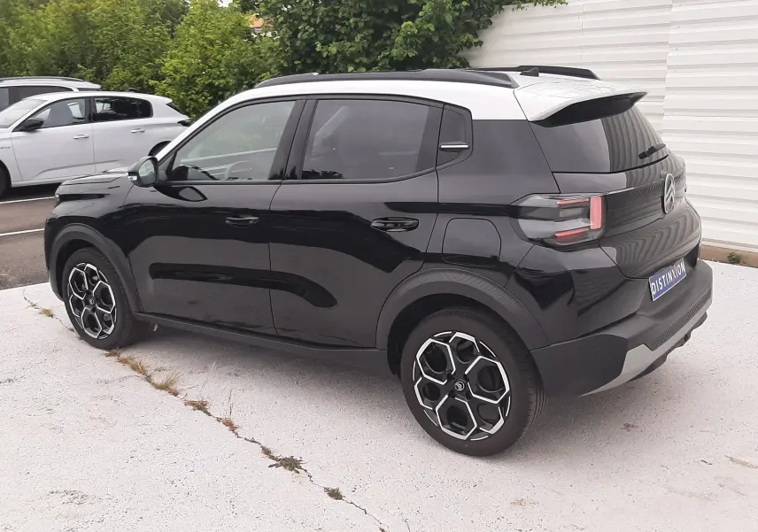 Vue 3/4 arrière droite d'une Citroën C3 2025 noir perla avec toit blanc et jantes biton distinctives.