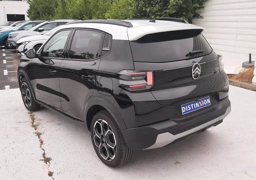 Vue 3/4 arrière droite d'une Citroën C3 2025 noir perla avec toit blanc, feux arrière LED et jantes biton.