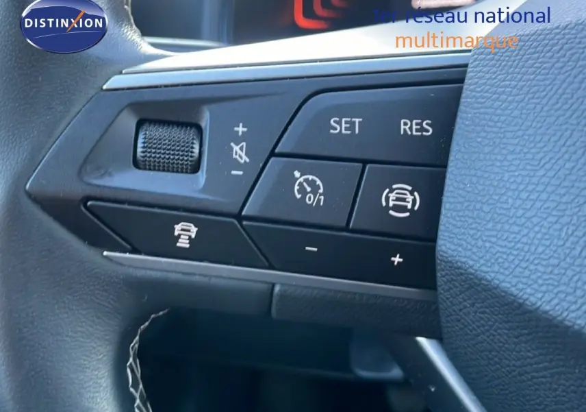 Gros plan sur les commandes au volant côté gauche du SEAT Arona blanc avec toit gris, montrant les boutons de régulateur de vitesse.