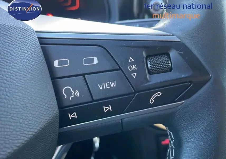 Gros plan sur les commandes au volant noir du SEAT Arona blanc avec toit gris, boutons multifonctions visibles.