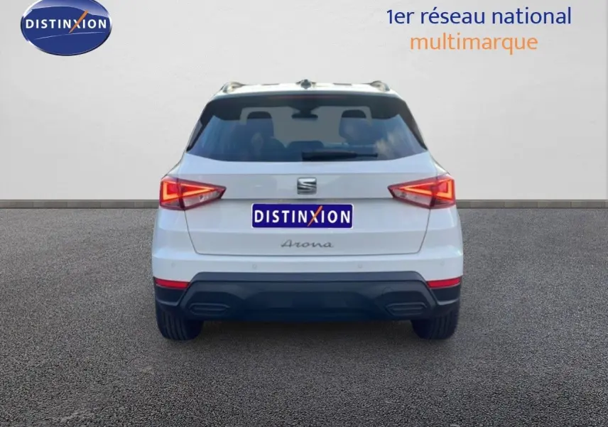 Vue arrière d'un SEAT Arona blanc avec toit gris, feux allumés et logo Distinxion visible sur fond neutre.