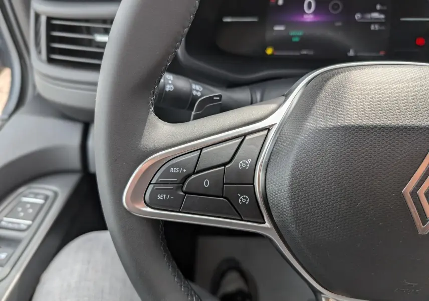 Gros plan sur le volant noir du Renault Trafic Fourgon 2025 avec commandes de régulateur de vitesse et tableau de bord numérique.