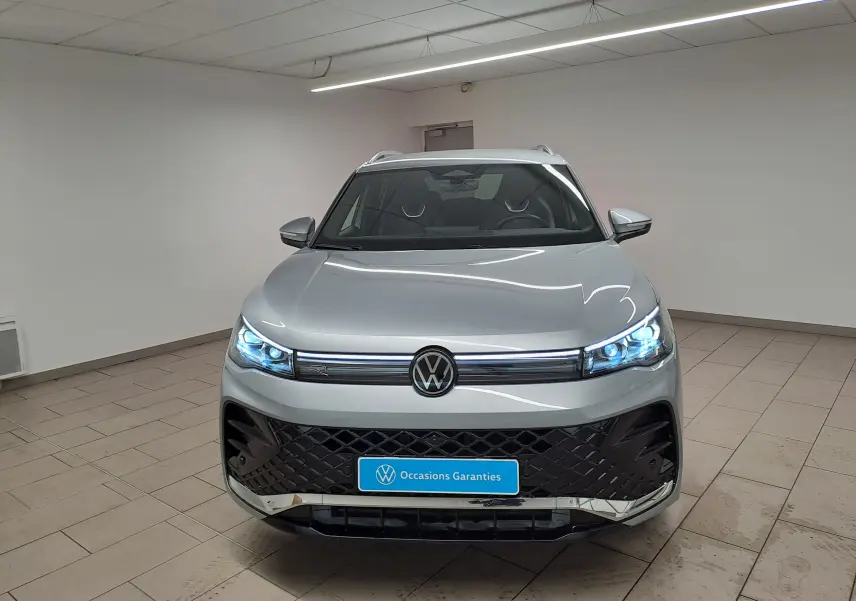 Vue avant d'un Volkswagen Tiguan 2.0 TDI 150 DSG7 R-Line en argent Dolomite avec phares LED allumés dans un showroom.