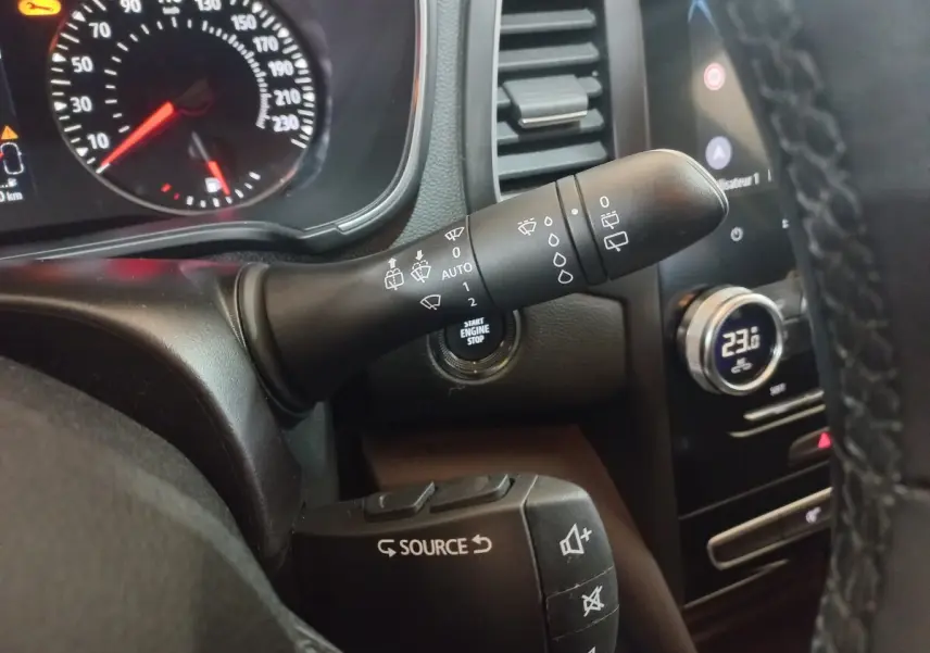 Gros plan sur les commandes au volant et tableau de bord d’une Renault Mégane Business gris foncé, avec affichage digital et bouton start.
