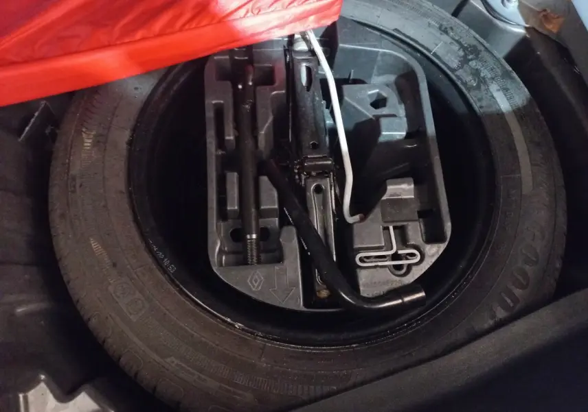 Vue rapprochée du coffre montrant la roue de secours et les outils de changement sur une Renault Mégane gris foncé.