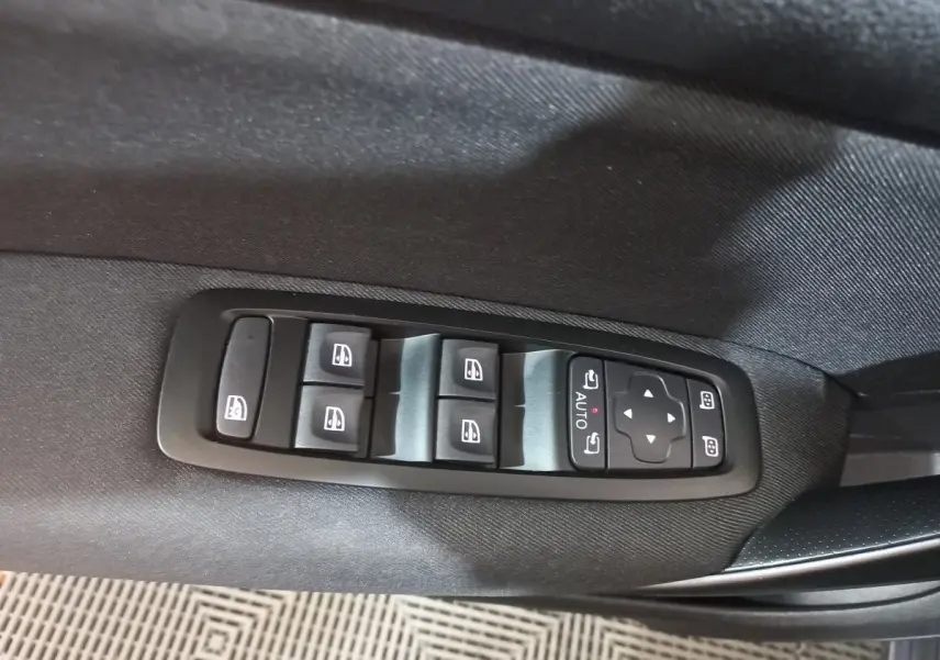 Vue rapprochée des commandes des vitres électriques et des rétroviseurs sur la porte côté conducteur d’une Renault Mégane gris foncé.