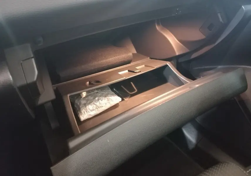 Gros plan sur la boîte à gants ouverte de la Renault Mégane Business gris foncé, montrant un rangement intérieur avec un objet emballé.