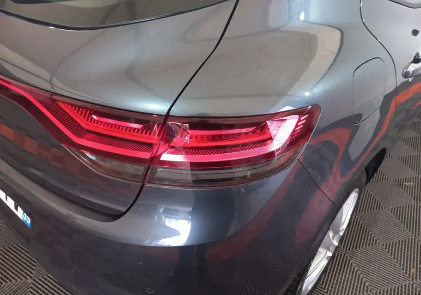 Vue 3/4 arrière droite d'une Renault Mégane Business gris foncé, mettant en valeur le feu arrière LED et la carrosserie brillante.