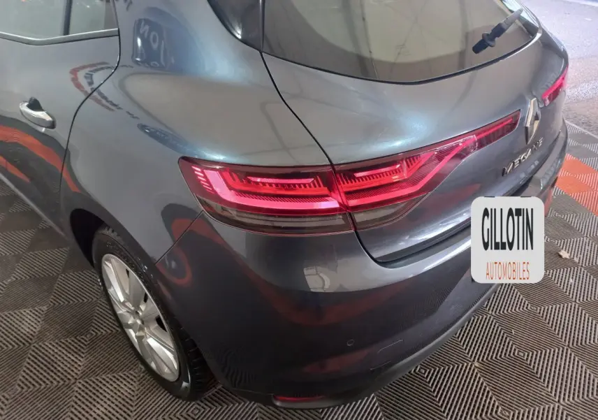 Vue 3/4 arrière droite d'une Renault Mégane Business gris foncé avec feux arrière LED allumés dans un garage.