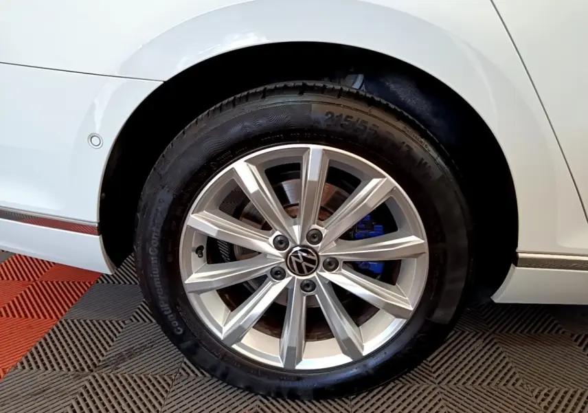 Gros plan sur la roue avant droite d'une Volkswagen Passat blanche avec jante alliage et étrier de frein bleu visible.