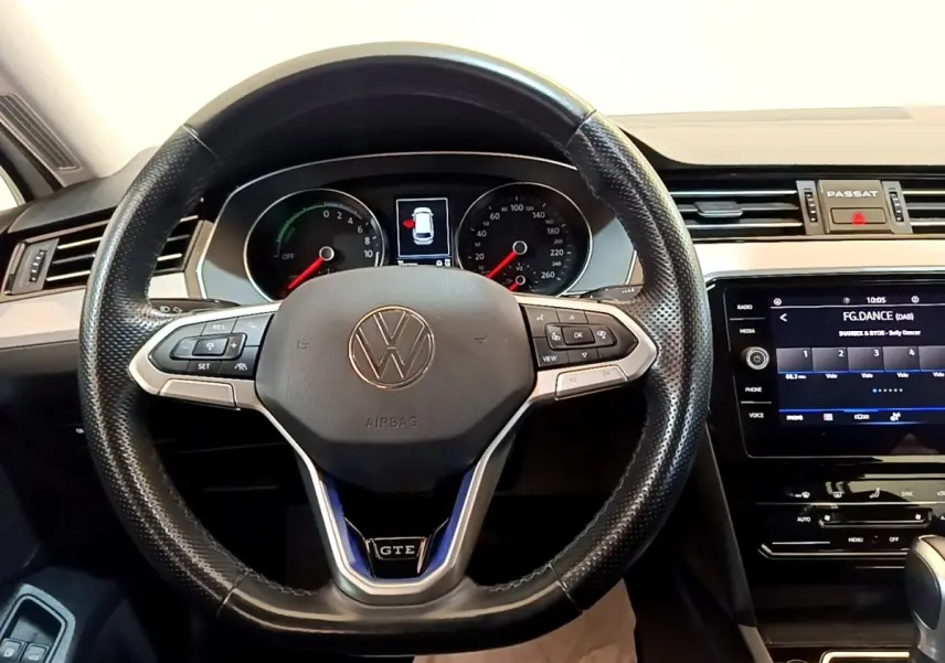 Vue intérieure centrée sur le volant cuir noir de la Volkswagen Passat GTE avec tableau de bord digital et écran tactile.
