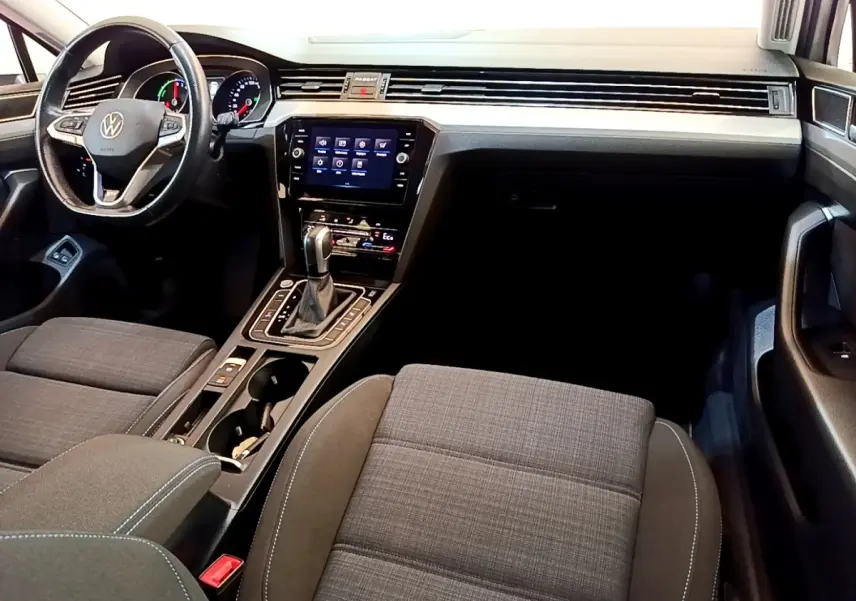 Vue intérieure avant droite de la Volkswagen Passat hybride avec tableau de bord noir, écran tactile et sièges tissu gris.