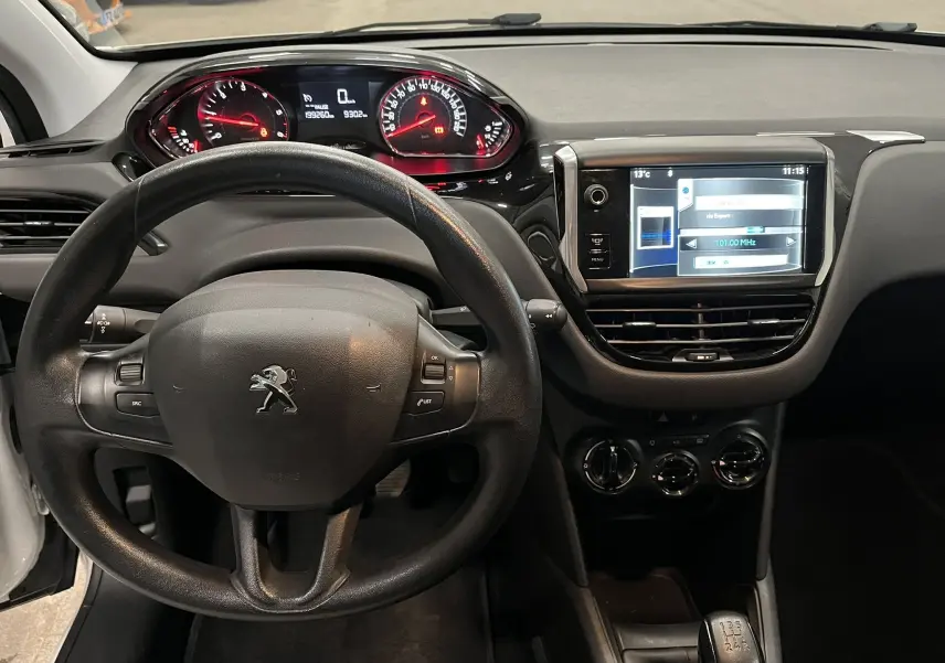 Vue intérieure du tableau de bord et volant noir de la Peugeot 208 blanche, avec écran tactile et compteurs rouges.
