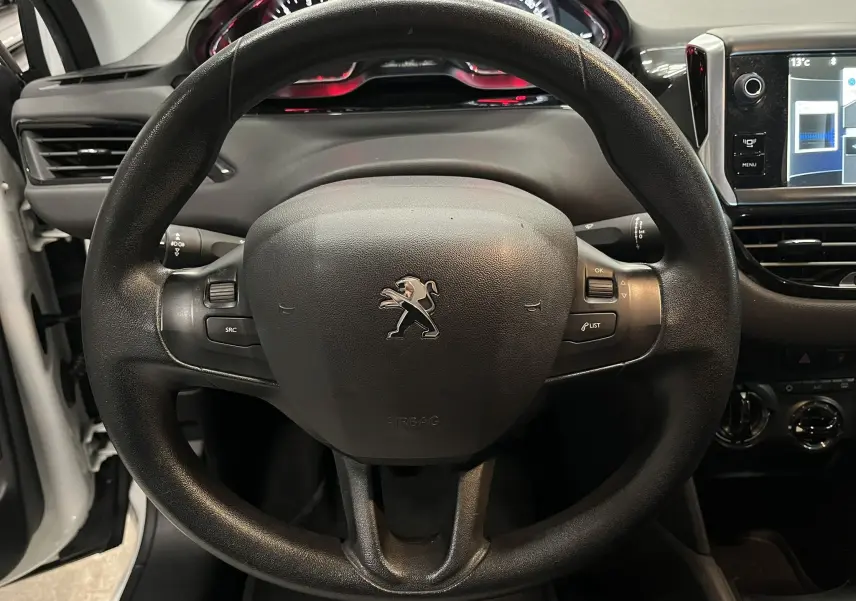Vue rapprochée du volant noir de la Peugeot 208 blanche de 2014, avec tableau de bord et écran tactile visibles.
