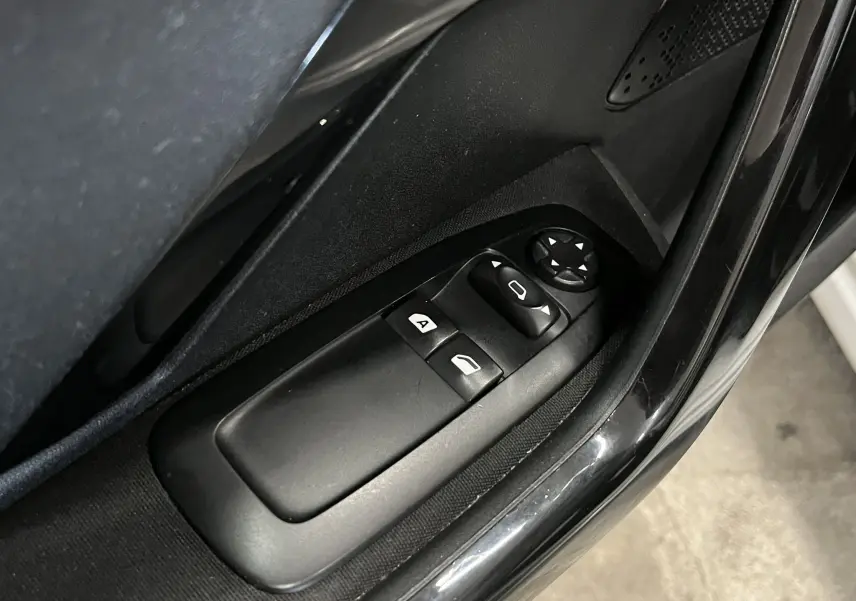 Gros plan sur les commandes de lève-vitres et réglage des rétroviseurs côté conducteur d'une Peugeot 208 blanche de 2014.