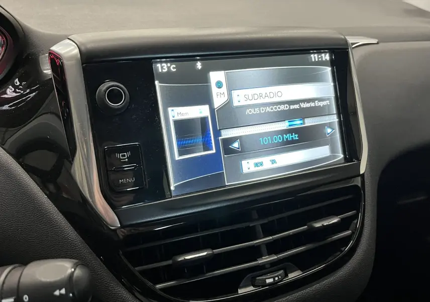 Vue rapprochée de l’écran tactile central noir de la Peugeot 208 blanche, affichant la radio FM à 101 MHz.