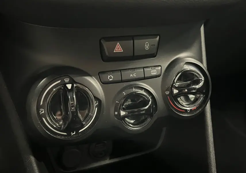Gros plan sur les commandes de climatisation noires de la Peugeot 208 blanche, avec boutons de réglage et ventilation.
