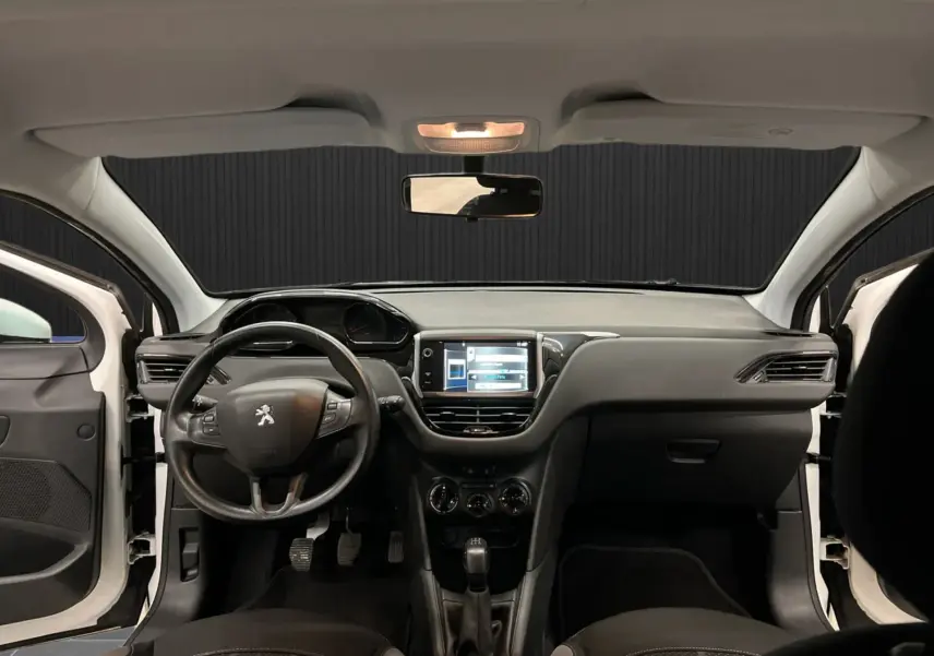 Vue intérieure avant du tableau de bord noir et volant multifonction d'une Peugeot 208 blanche avec portes ouvertes.