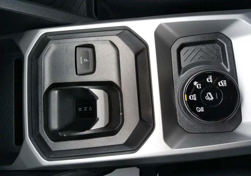 Vue rapprochée de la console centrale grise du Dacia Duster Hybrid-G 150 ch, avec sélecteur de boîte auto et molette de modes de conduite.