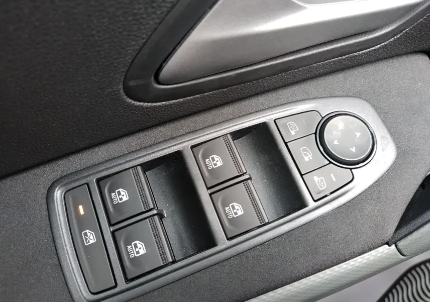 Gros plan sur les commandes des vitres électriques et rétroviseurs côté conducteur du Dacia Duster Hybrid-G couleur Sandstone.