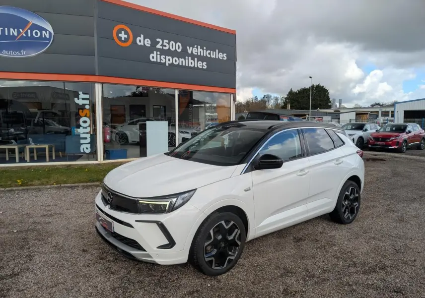 Opel Grandland blanc métallisé en 3/4 avant droit avec toit noir et jantes alliage noires sur parking.