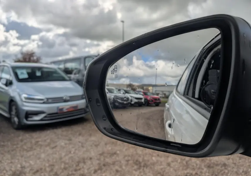 Rétroviseur côté droit d’un Opel Grandland blanc métallisé, vue partielle du véhicule et parking en arrière-plan.