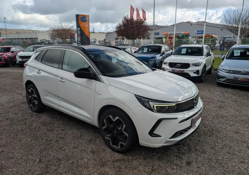 Opel Grandland blanc métallisé en 3/4 avant droit avec toit noir et jantes alliage noires sur parking.