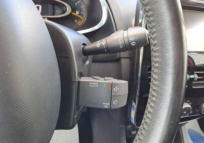 Gros plan sur la commande audio au volant côté gauche d’une Renault Clio IV rouge, avec levier d’essuie-glace visible.