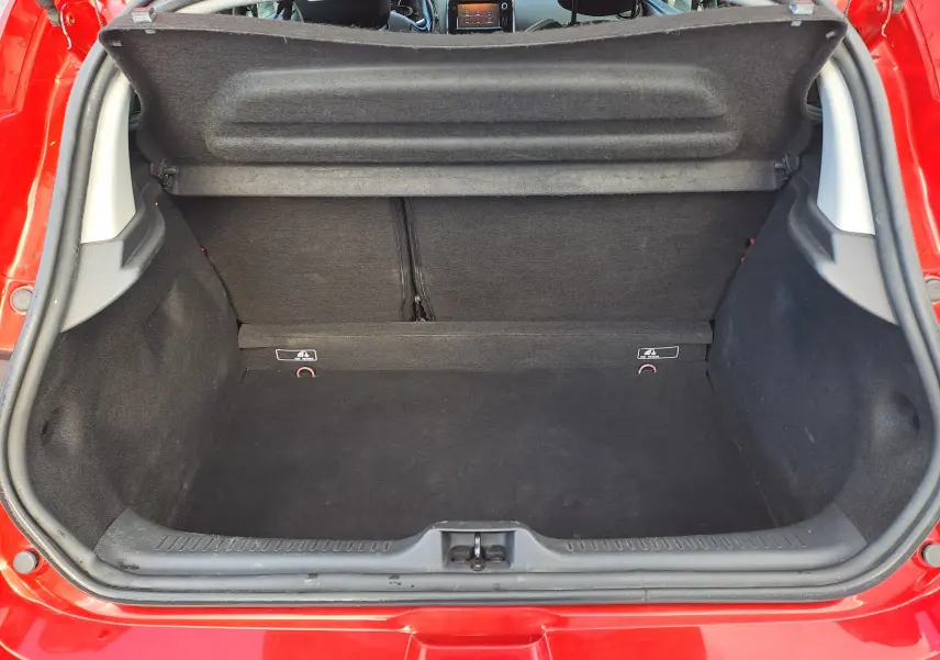 Coffre ouvert vu de l'arrière d'une Renault Clio IV rouge, montrant l'espace de chargement vide et la plage arrière relevée.