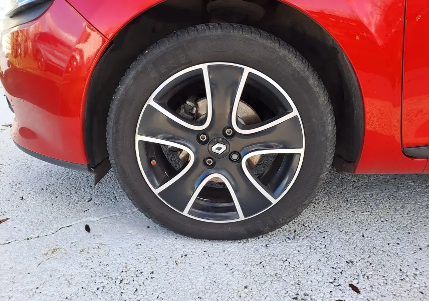 Gros plan sur la roue avant gauche d'une Renault Clio IV rouge avec jante alliage noire et argentée.