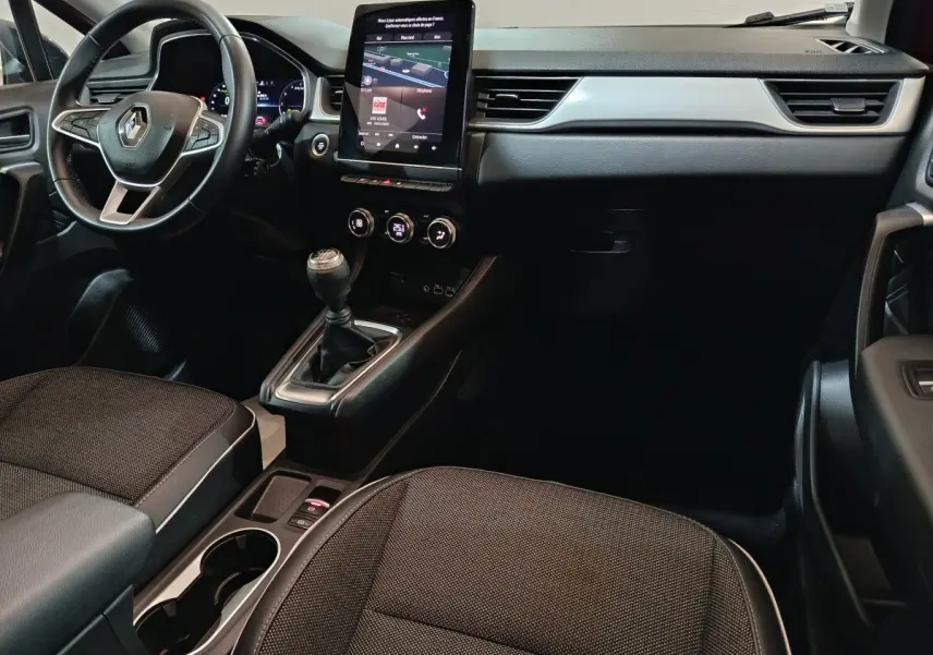 Vue intérieure avant droite du Renault Captur 2024 essence rouge, avec tableau de bord moderne et écran tactile vertical.