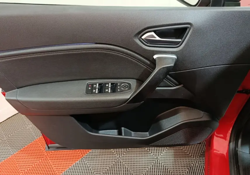 Vue intérieure côté gauche de la porte avant rouge du Renault Captur 2024 avec commandes de vitres et poignée noire.