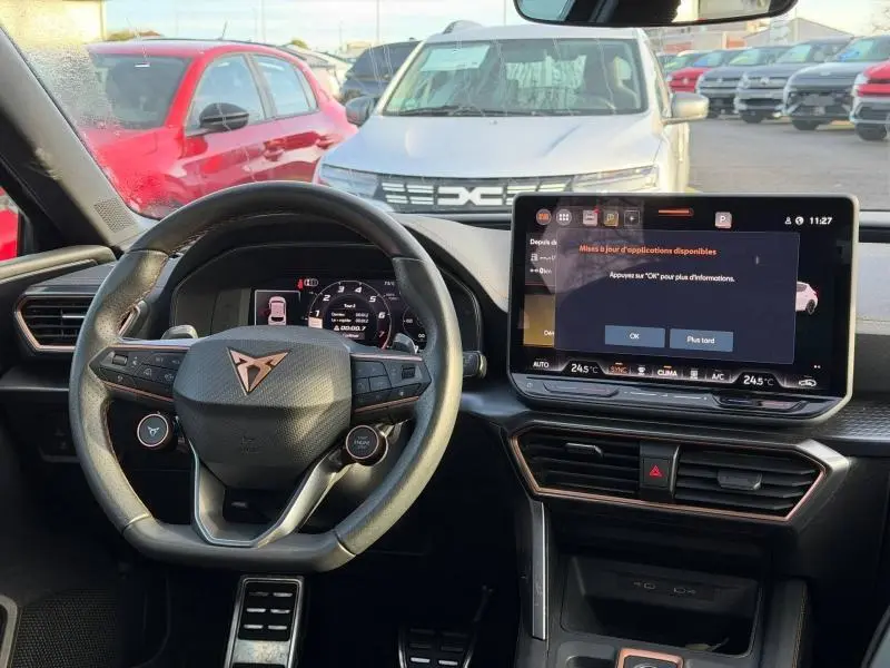 Vue intérieure du poste de conduite d'une SEAT Leon 1.5 eTSI Hybrid 2025, avec volant multifonction et écran tactile central allumé.