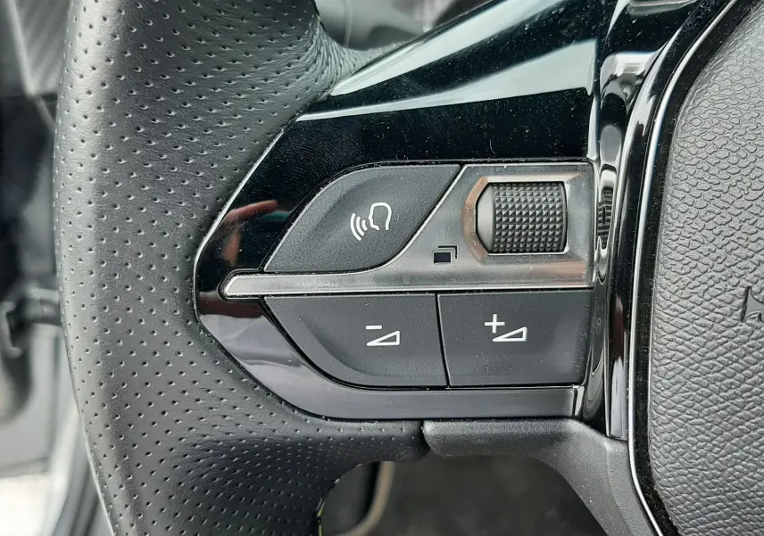 Gros plan sur les commandes gauche du volant perforé de la Peugeot 208 1.2 100CH GT, finition noire brillante.