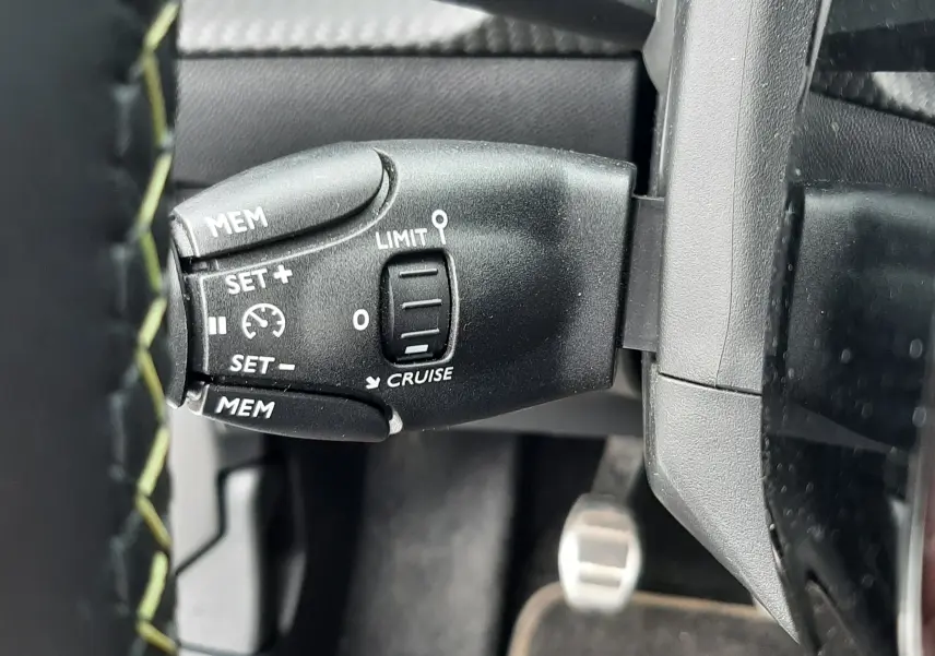 Gros plan sur la commande de régulateur de vitesse à gauche du volant dans un Peugeot 208 gris Artense 2025.