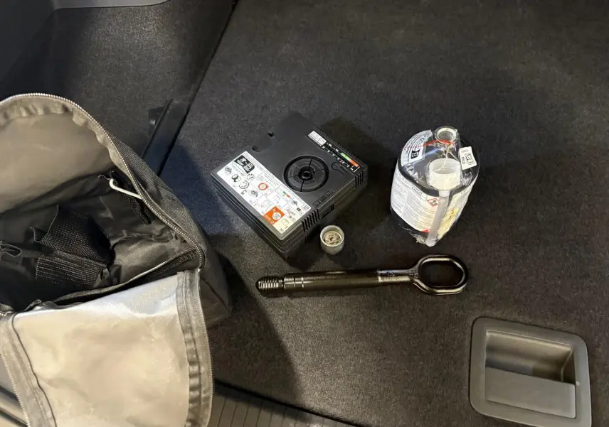 Vue rapprochée du coffre d’un Volkswagen Tiguan 2.0 TDI gris Dauphin, montrant les outils de dépannage rangés au sol.