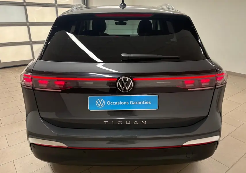 Vue arrière du Volkswagen Tiguan 2025 gris dauphin avec feux LED allumés et logo VW bien visible.