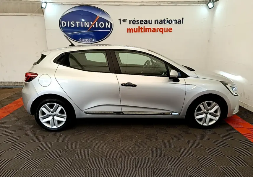 Profil droit d'une Renault Clio Business TCe 100 gris clair, stationnée en intérieur sur sol damier noir et rouge.